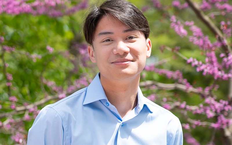 Aidan Collins wearing a blue shirt and smiling outside.
